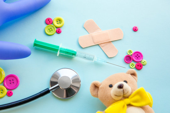 Children vaccination concept. Syringe surrounded with different medical tools and children toys, blue background, flat lay view.