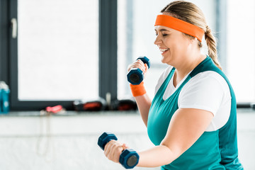 plus size woman exercising with dumbbells and laughing in gym