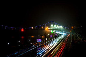 Fototapeta na wymiar Glowing footbridge in the night fog and headlights of cars. Kyiv. Ukraine