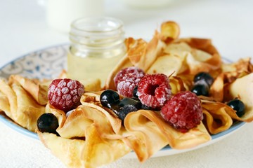Homemade thin pancakes with berries, honey and milk for breakfast on a light background. Traditional cuisine. Pancake week. Shrovetide Maslenitsa Butter Week festival meal.