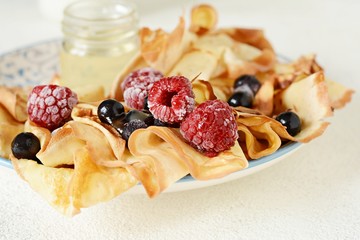 Homemade thin pancakes with berries, honey and milk for breakfast on a light background. Traditional cuisine. Pancake week. Shrovetide Maslenitsa Butter Week festival meal.