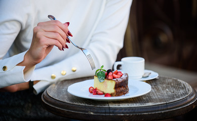 Appetite concept. Dessert cake cup of coffee and female hand with fork close up. Piece of cake with red berry. Gourmet recipe food. Cake slice on white plate. Cake with cream delicious dessert