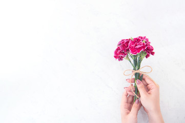 May mothers day idea concept photography - Beautiful blooming carnations tied by rope bow holding in woman's hand isolated on bright modern table, copy space, flat lay, top view