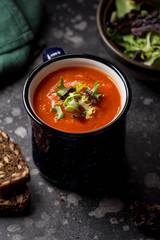 Orange vegetable cream soup in mug (tomato, carrot, lentil, pumpkin), delicious hot homemade lunch in cup. Dark background