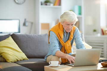 Portrait of contemporary senior man using laptop at home and looking thoughtful, copy space