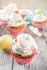 Easter kids party treat. Festive Easter food. Homemade cupcakes with cream and marshmallow cute bunny rabbits with paws. On a white wooden table, top view copy space