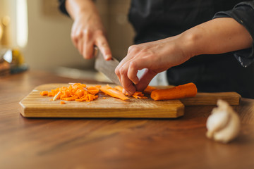 Female chef chopping carrots  on a wooden board