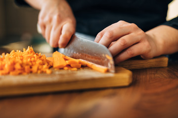 Female chef chopping carrots  on a wooden board