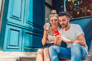 Mixed race couple in love walking in city. Arab man and white woman drinking coffee and using smartphone