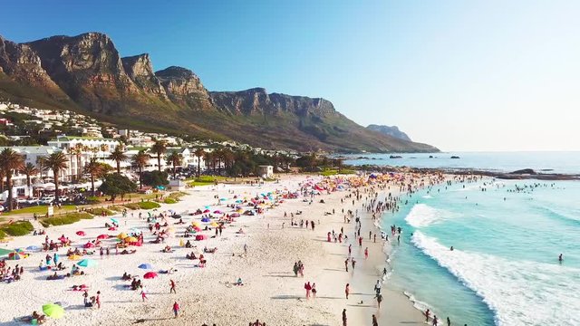 Spectacular aerial over a crowded and busy holiday beach at Camps Bay, Cape Town, South Africa with Twelve Apostles mountains background.