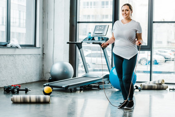 cheerful plus size woman standing with jumping rope in gym - obrazy, fototapety, plakaty