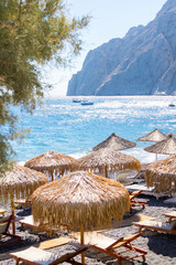 beach with umbrellas and deck chairs by the sea in Santorini