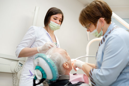 Dentist with nurse doing dental treatment of senior male patient in dental clinic. Dental care for elder people. Dentistry, medicine and health care concept