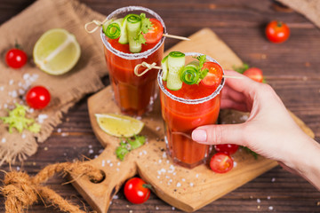 Two glasses of tomato juice decorated with fresh tomatoes, cucumber and leaves on a wooden background