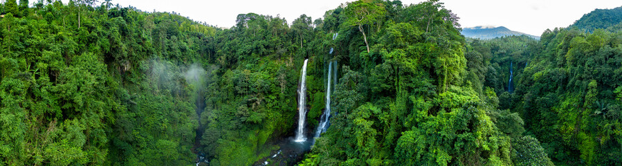 Aerial over Sekumpul waterfall surrounded by dense rainforest and mountains shrouded in mist at sunrise, Bali, Indonesia panoramic - obrazy, fototapety, plakaty