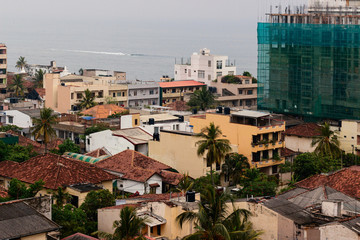 Fototapeta premium Aerial drone shoot above the architecture of Colombo, Sri Lanka. Modern and antuque houses. Ocean beach on horizon. New buildings, ghetto, garbage and tiled roofs.
