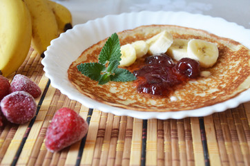 freshly fried homemade french crepes on a plate with strawberries, banana slices and fresh cream, horizontal view from above, close-up