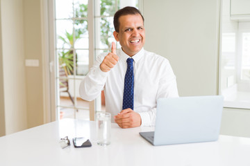 Middle age business man working with computer laptop doing happy thumbs up gesture with hand. Approving expression looking at the camera with showing success.