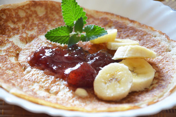 freshly fried homemade french crepes on a plate with strawberries, banana slices and fresh cream, horizontal view from above, close-up