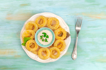 A plate of squid rings, shot from above on a blue background with a fork and copy space