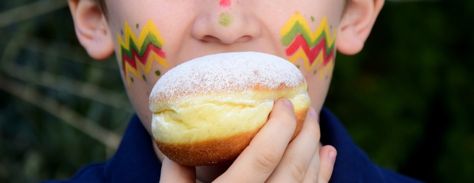 Ein als Indianer geschminktes Kind isst einen Faschingskrapfen