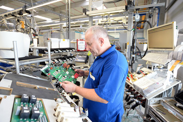 älterer Elektriker bei der Montage von elektronik in einer modernen Fabrik im Maschinenbau //...