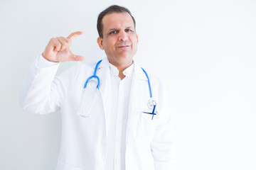 Fototapeta premium Middle age doctor man wearing stethoscope and medical coat over white background smiling and confident gesturing with hand doing size sign with fingers while looking and the camera. Measure concept.