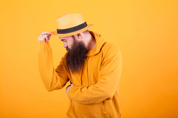 Attractive bearded man touching his hat over yellow background