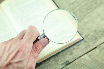 Man using magnifying glass for reading the book.