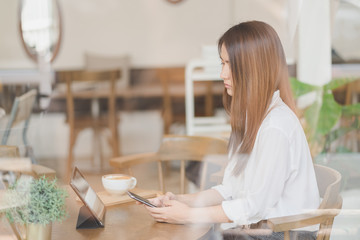 Young attractive Asian woman is using tablet and smartphone in coffee shop cafe, online content background with copy space.