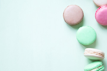 Colorful macaron or macaroon cakes on pastel green background with copy space.
