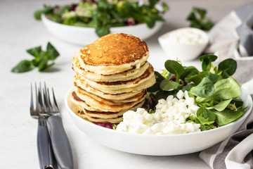 Savory pancakes with cheese served with green salad mix and fresh farm cottage cheese. Healthy breakfast or lunch. Light concrete background. Copy space.