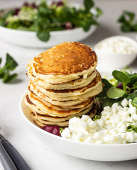 Savory pancakes with cheese served with green salad mix and fresh farm cottage cheese. Healthy breakfast or lunch. Light concrete background. Copy space.