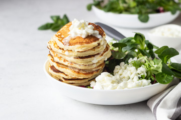 Savory pancakes with cheese served with green salad mix and fresh farm cottage cheese. Healthy breakfast or lunch. Light concrete background. Copy space.