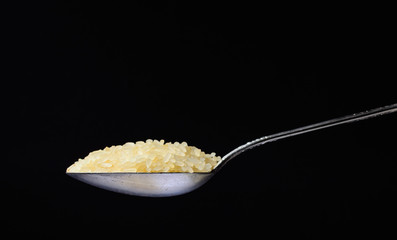 Raw rice poured into a silver spoon. Side view on a black background. Minimalism and space for text.