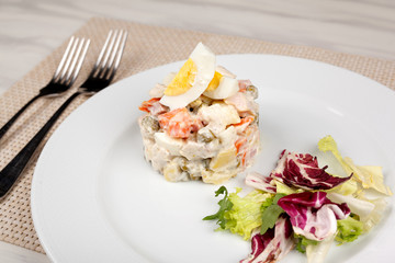 Salad Olivier with egg and cabbage on a white plate.