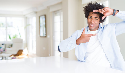 Obraz premium African American man at home smiling making frame with hands and fingers with happy face. Creativity and photography concept.