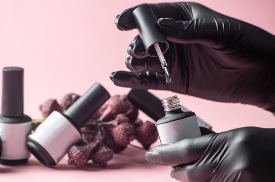 Nail salon: the master's hand in a black glove is dipping a brush with a drop in nail polish.