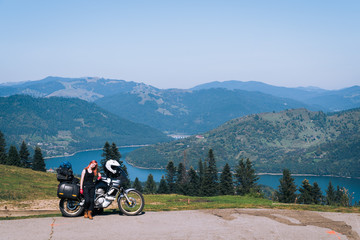woman biker with adventure motorcycle on road, Ceahlau mountains, Romania, tourism travel concept, motorcyclists way, copy space, lake Lzvorul Muntelui, beautiful sunny day