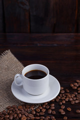 White cup of coffee with coffee grains near on linen fabric on the dark vintage background. Vertical photo