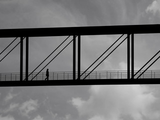 The Silhouette of A Woman Walking On A Bridge Against A Cloudy Sky