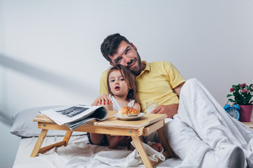 Father and daughter having breakfast in bed in the morning