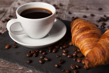 Cup of coffee and spreaded coffee beans with fresh croissants