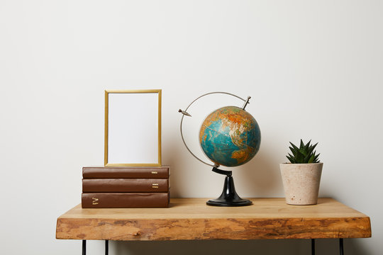 Frame on books near globe and green plant in pot