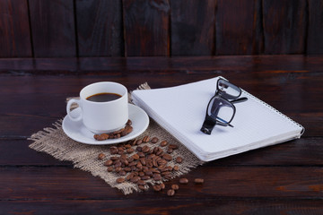 White coffee cup with notepad and glasses on a dark wooden background and linen fabric
