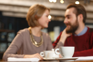 Warming moments. Selective focus on the cup of coffee on the cafe table loving couple talking on the background