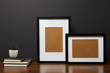 black square frames near books and plant on wooden table