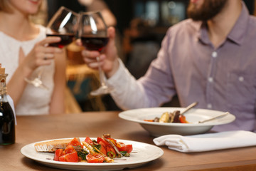Cheers! Selective focus on delicious food on the restaurant table couple cheering with wine glasses on the background