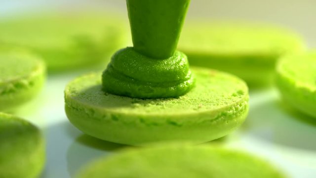 Making green pistachio macarons, squeezing and adding cream filling from pastry bag. Macaroons - delicious and beautiful french dessert. Cooking, food and baking, pastry concept.