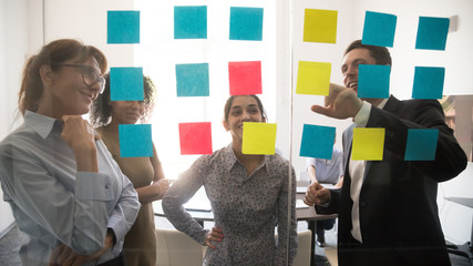 Diverse team people looking at sticky notes on glass brainstorming